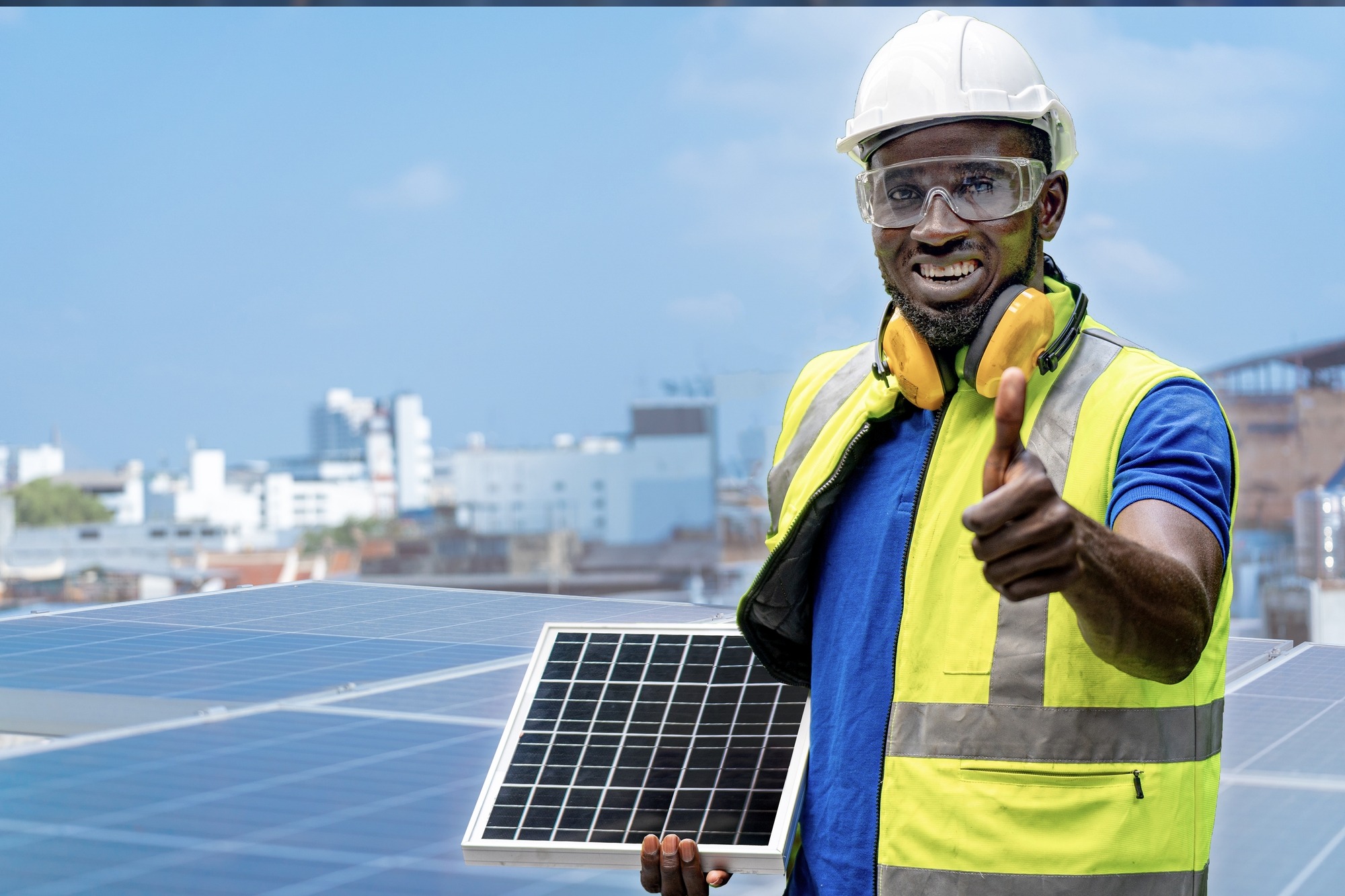 African Worker Holding Solar Cell Panel and Standing Confidence at Rooftop of Solar Cell Panel in Background.